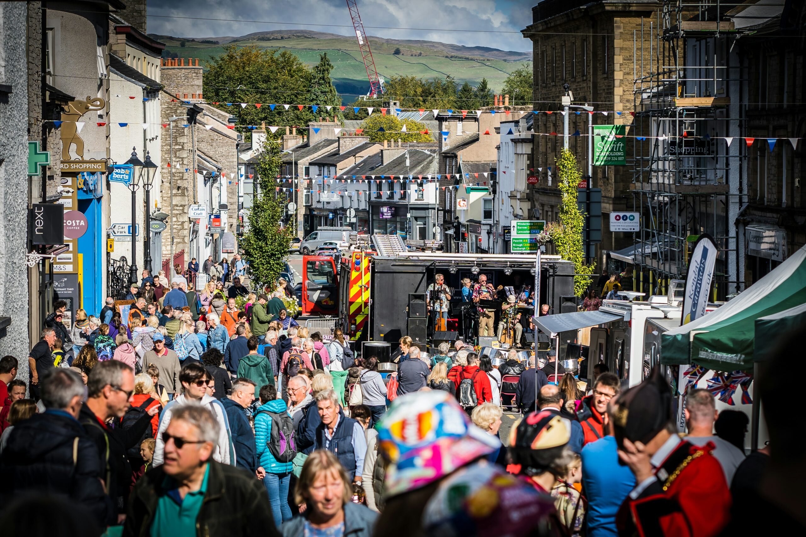 "Vibrant town center festival in Holbeach, featuring live music performances, colorful arts displays, food stalls, and a lively crowd enjoying a sunny day.